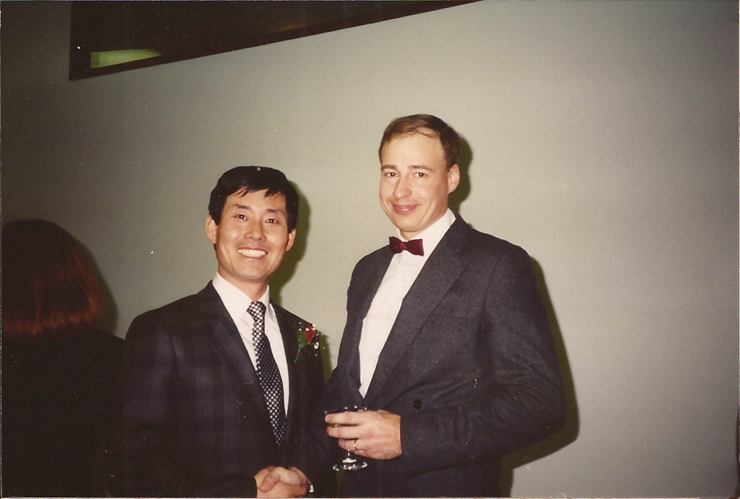 A student shakes a professor's hand while both smile at the camera. 